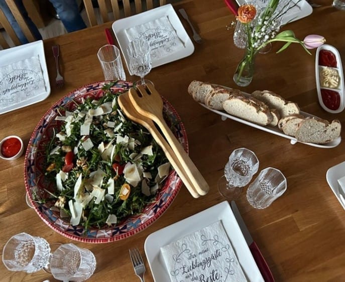 Gedeckter Holztisch mit Rucola-Salat, Brot und Blumen bei einem Running Dinner