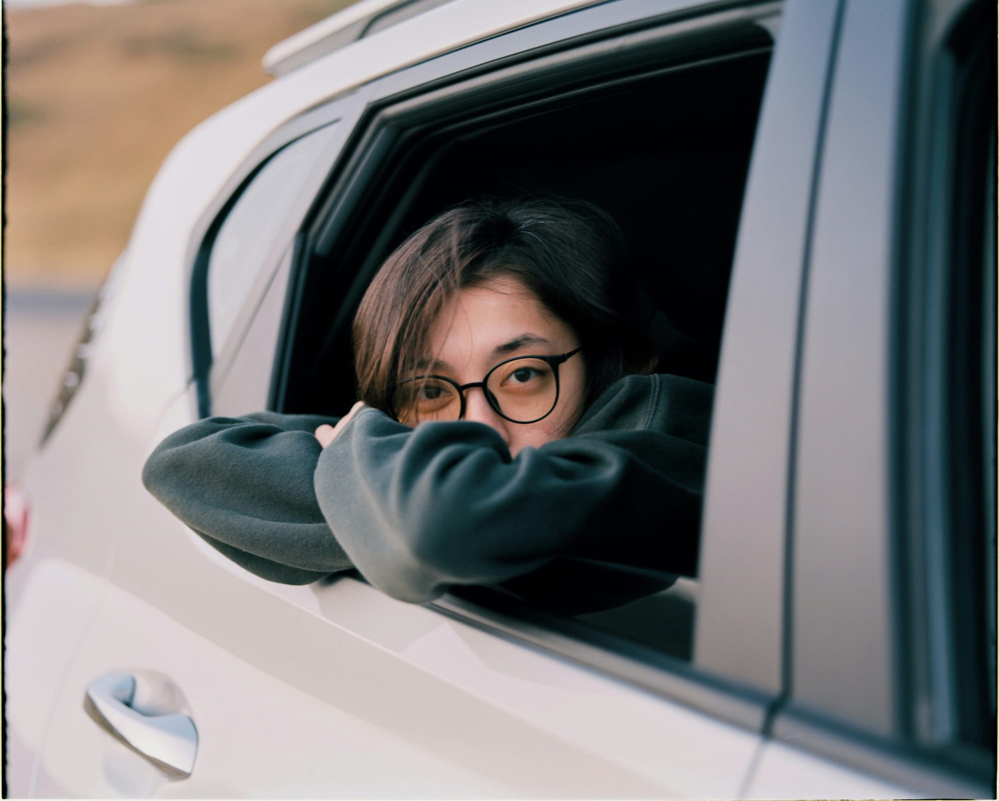 Junge Person mit Brille schaut zurückgezogen aus einem Autofenster.