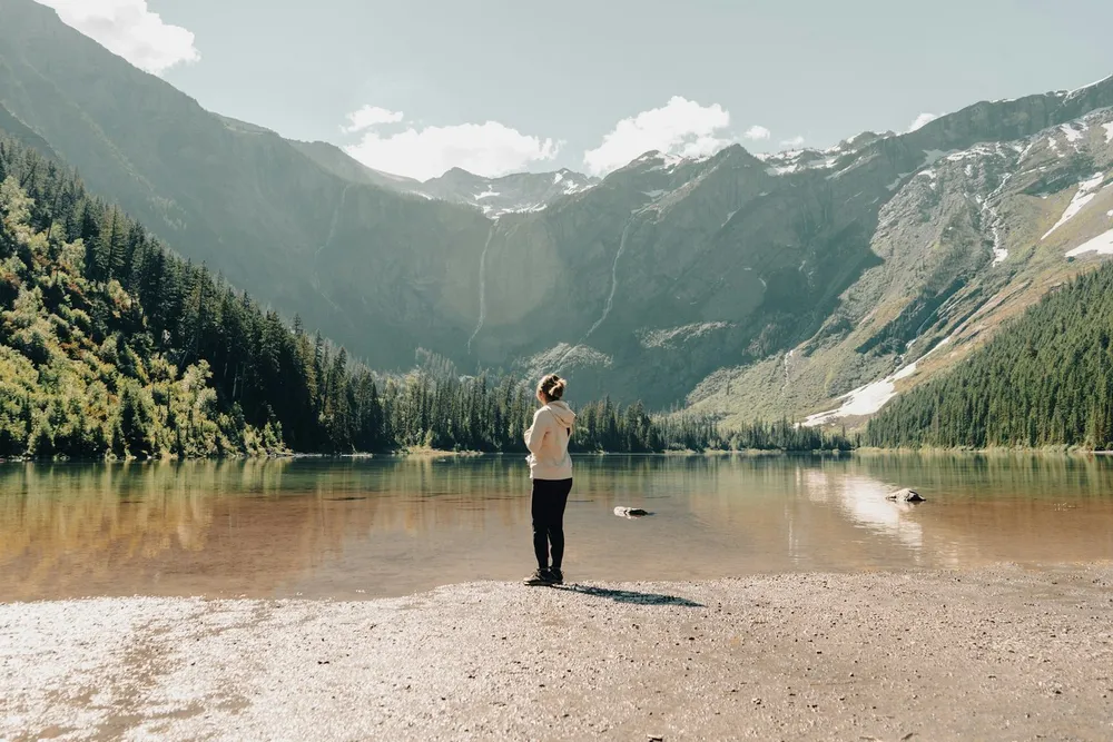 Junge Frau genießt mit offenen Armen den Blick auf einen Bergsee