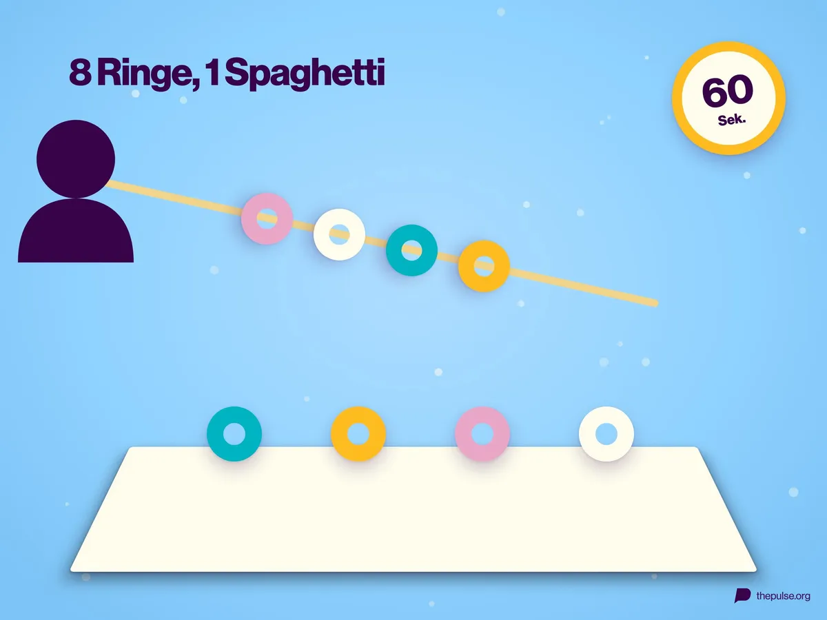 Eine rohe Spaghettinudel mit aufgefädelten Ringen, weitere Ringe stehen hochkant am Tischrand