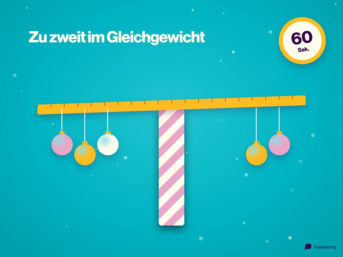 Eine Holzleiste balanciert auf einer gestreiften Geschenkpapierrolle, an beiden Enden hängen Weihnachtskugeln