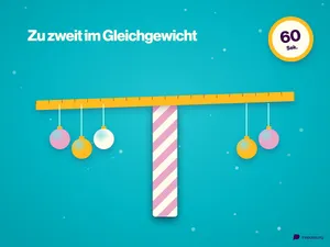 Eine Holzleiste balanciert auf einer gestreiften Geschenkpapierrolle, an beiden Enden hängen Weihnachtskugeln