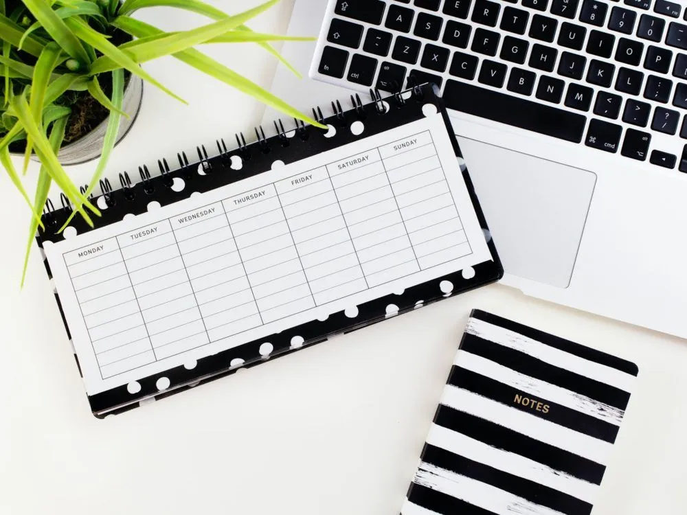 A weekly planner, a notebook and a keyboard on a white desk