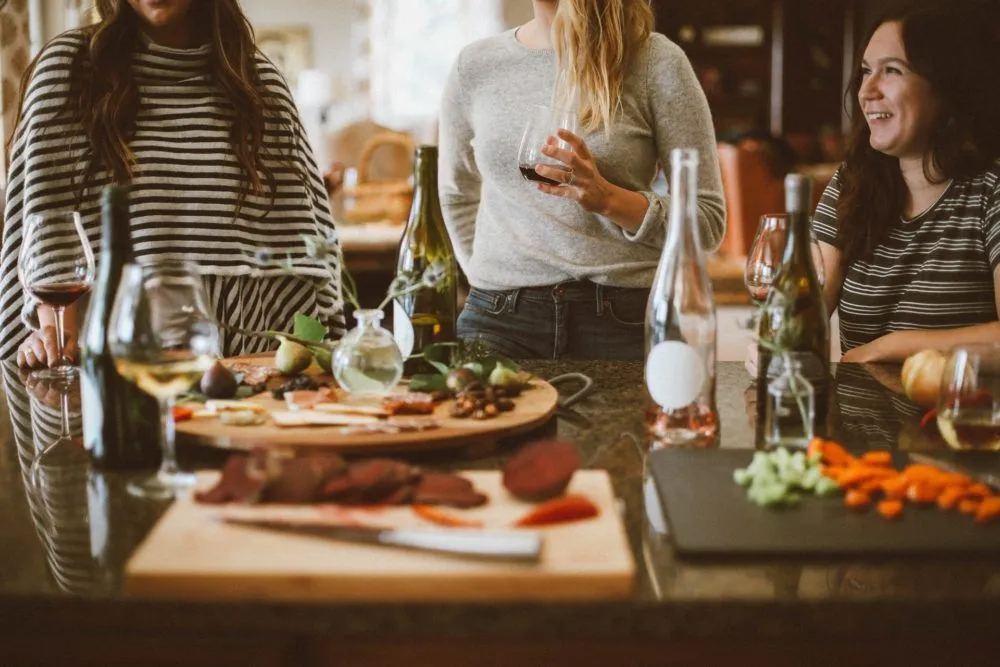 Three friends talking around a kitchen counter with snacks and drinks