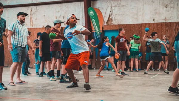 Teenagers in a camp hall playing a ball game; in front, a boy with a headband gets ready to throw
