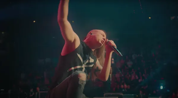 A rock singer on stage under red lights, one arm raised