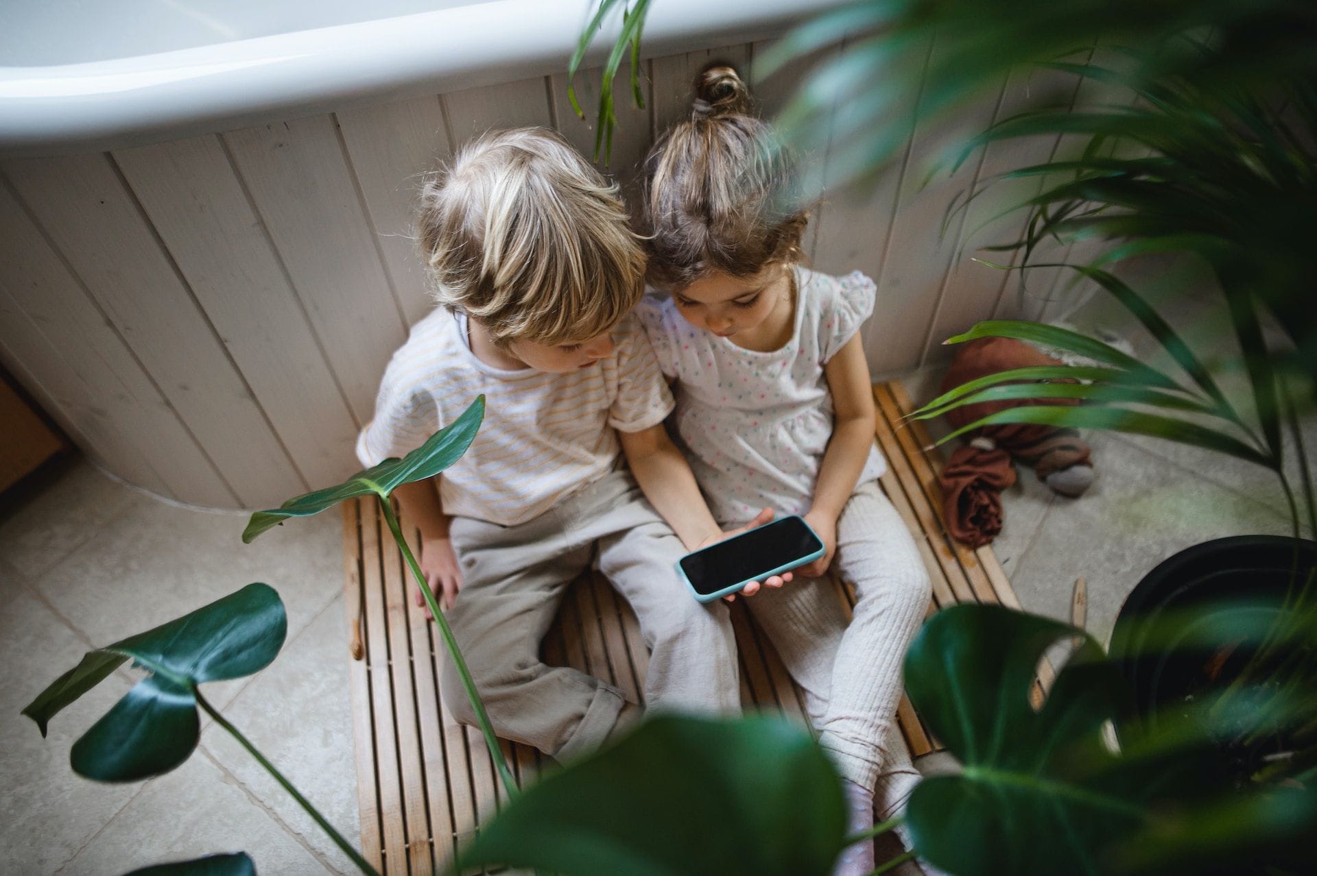 Dos niños pequeños, sentados en el suelo, miran juntos un teléfono