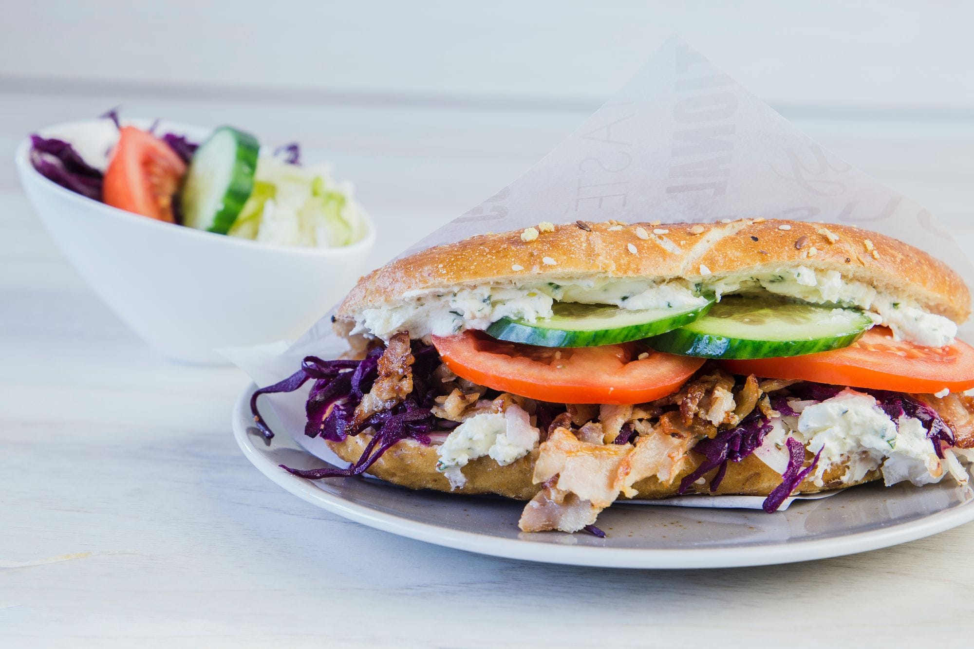 Un kebab en pan, relleno de carne y verduras, junto a un bol de ensalada