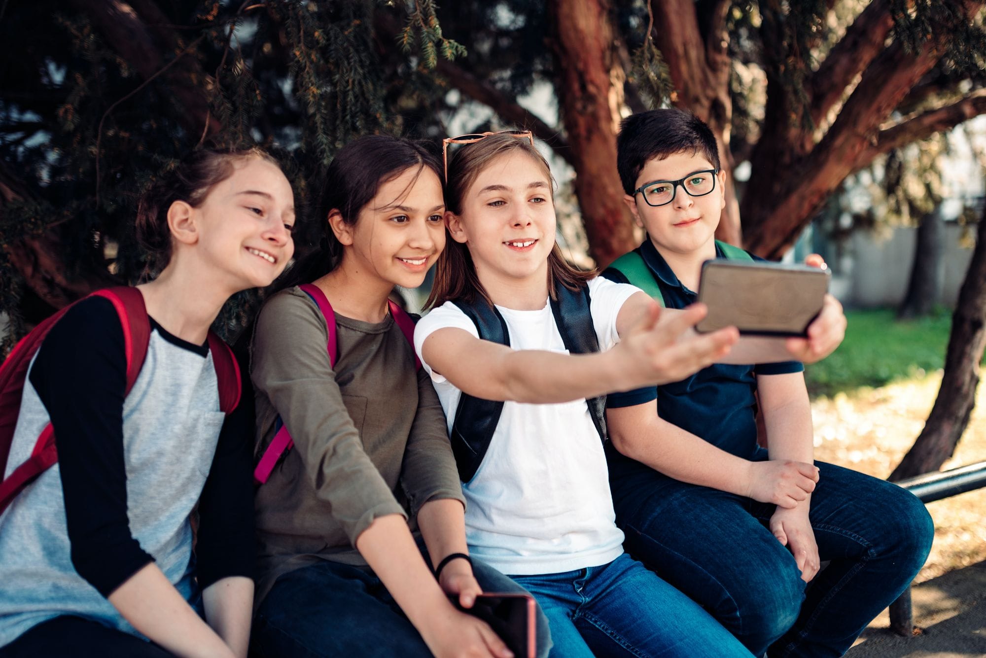 Cuatro preadolescentes con mochila posan juntos para una foto con un teléfono