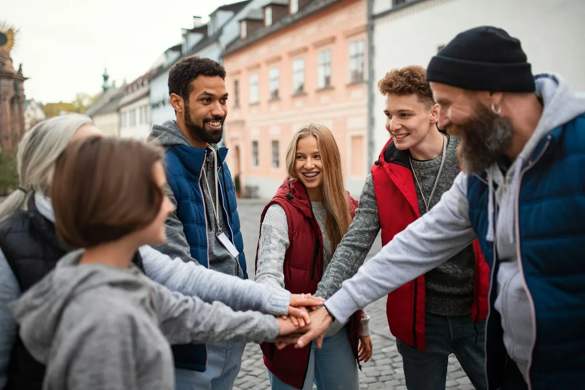 Jóvenes y adultos de distintas edades ponen las manos unas sobre otras, en círculo, en una calle, sonriendo