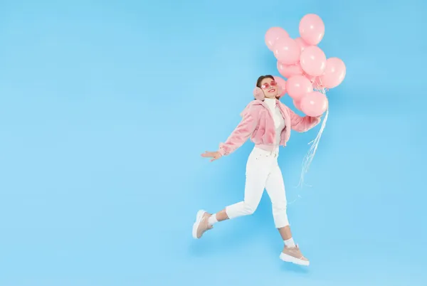 Una mujer joven salta con globos de color rosa en la mano