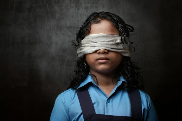 Un niño con una venda negra en los ojos, frente a un fondo oscuro