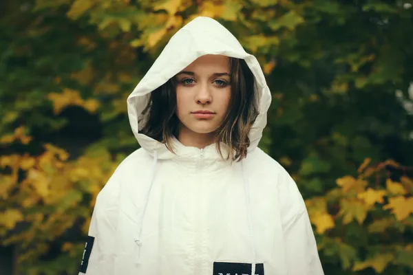 Una adolescente con un impermeable blanco con capucha, en otoño