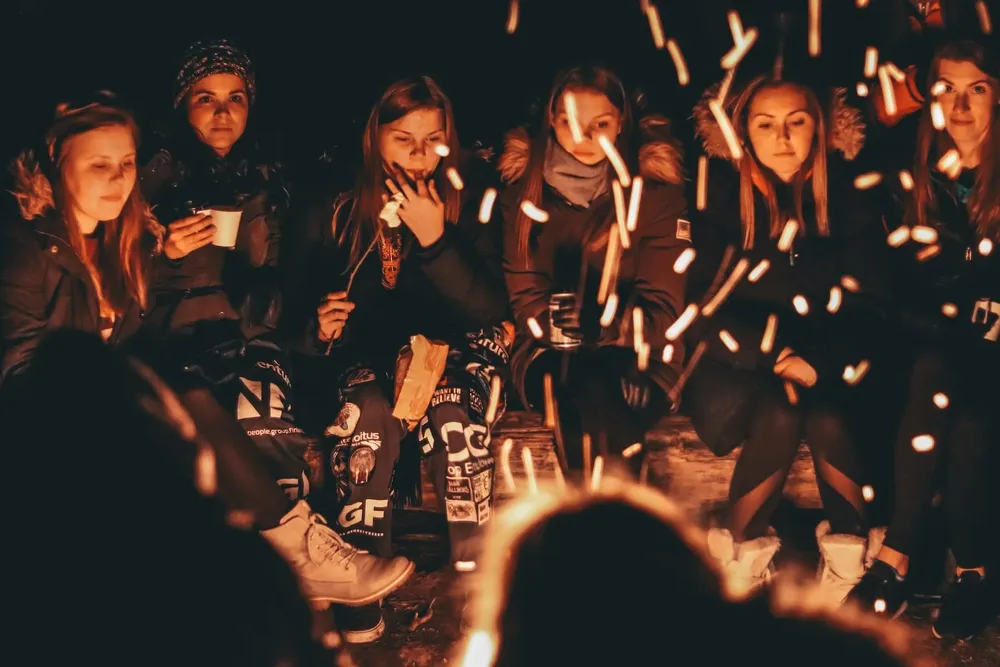 Des jeunes femmes assises de nuit autour d’un feu de camp, des étincelles volent devant elles