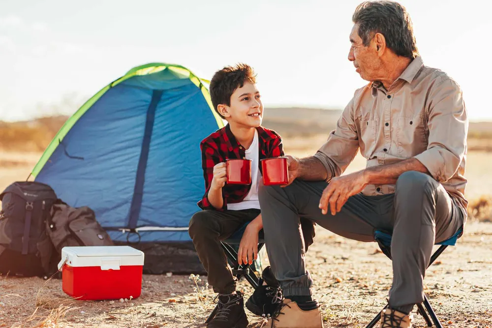 Un garçon et son grand-père, une tasse à la main, devant une tente