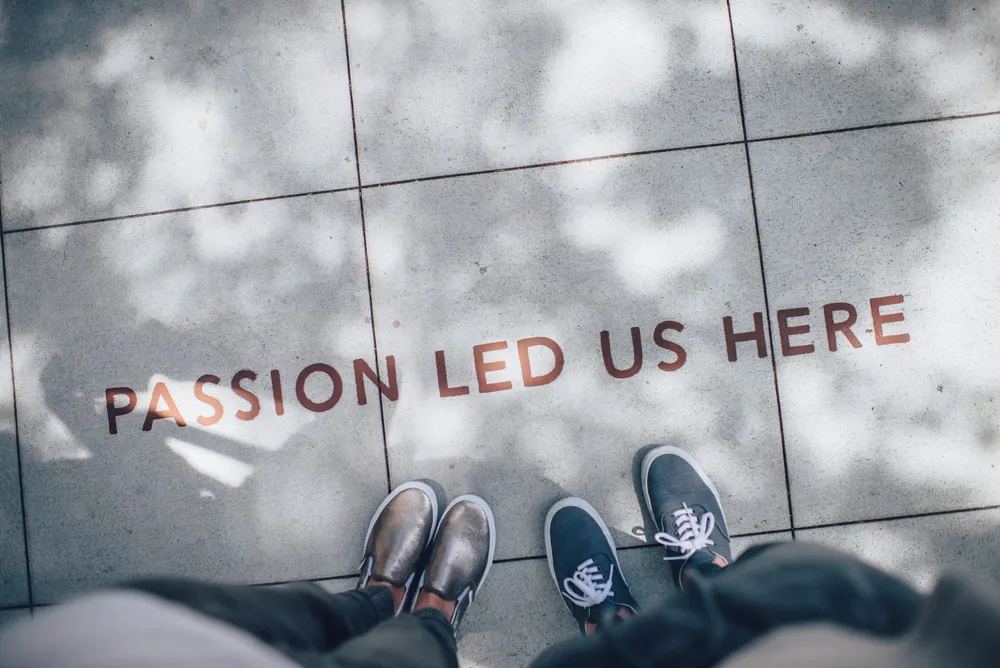 Les pieds de deux personnes sur un trottoir, à côté des mots peints « passion led us here »
