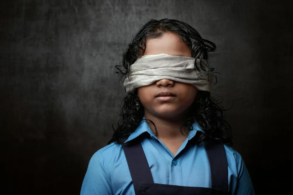 Un enfant avec un bandeau noir sur les yeux, devant un fond sombre