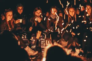Des jeunes femmes assises de nuit autour d’un feu de camp, des étincelles volent devant elles