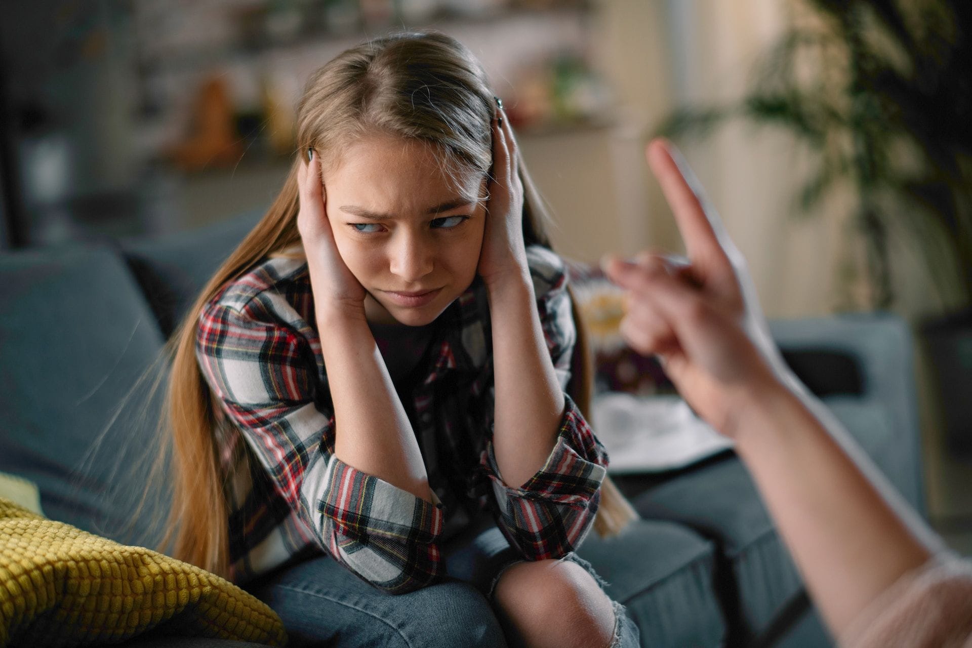 O adolescentă își acoperă urechile cu mâinile și se uită încruntată la un adult care ridică arătătorul spre ea