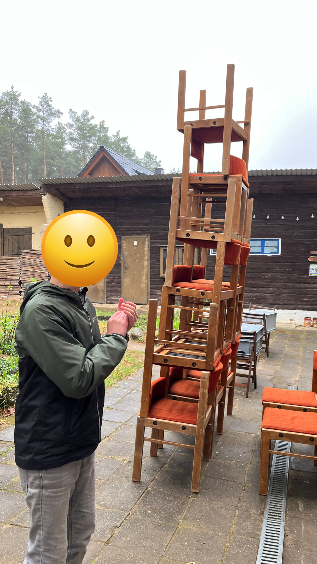 Un tânăr cu fața acoperită de un emoji zâmbitor, lângă un alt turn din scaune stivuite
