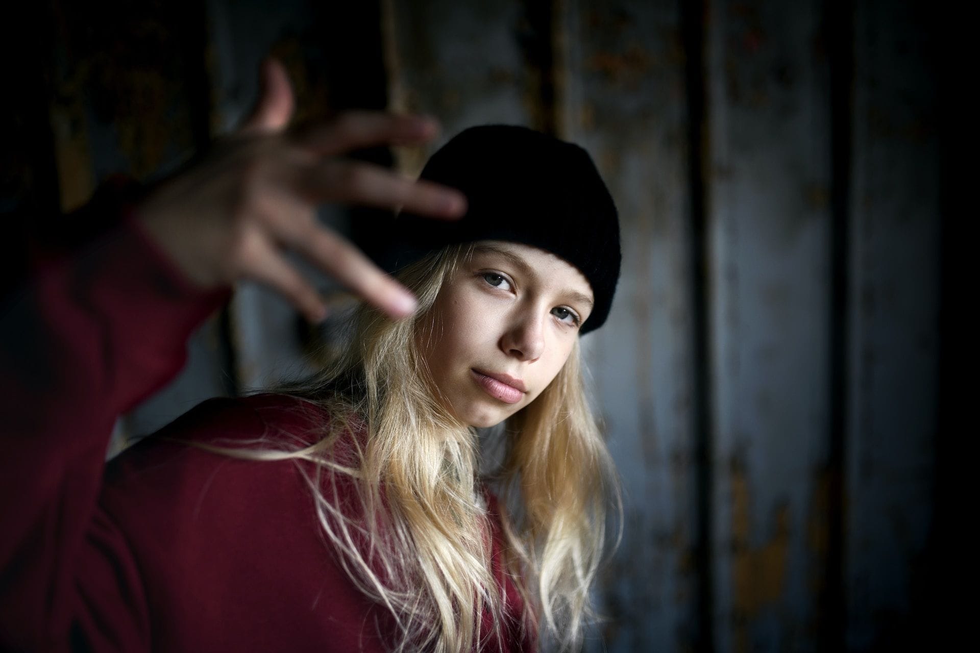 O adolescentă blondă, cu căciulă neagră, ține o mână ridicată spre aparatul de fotografiat