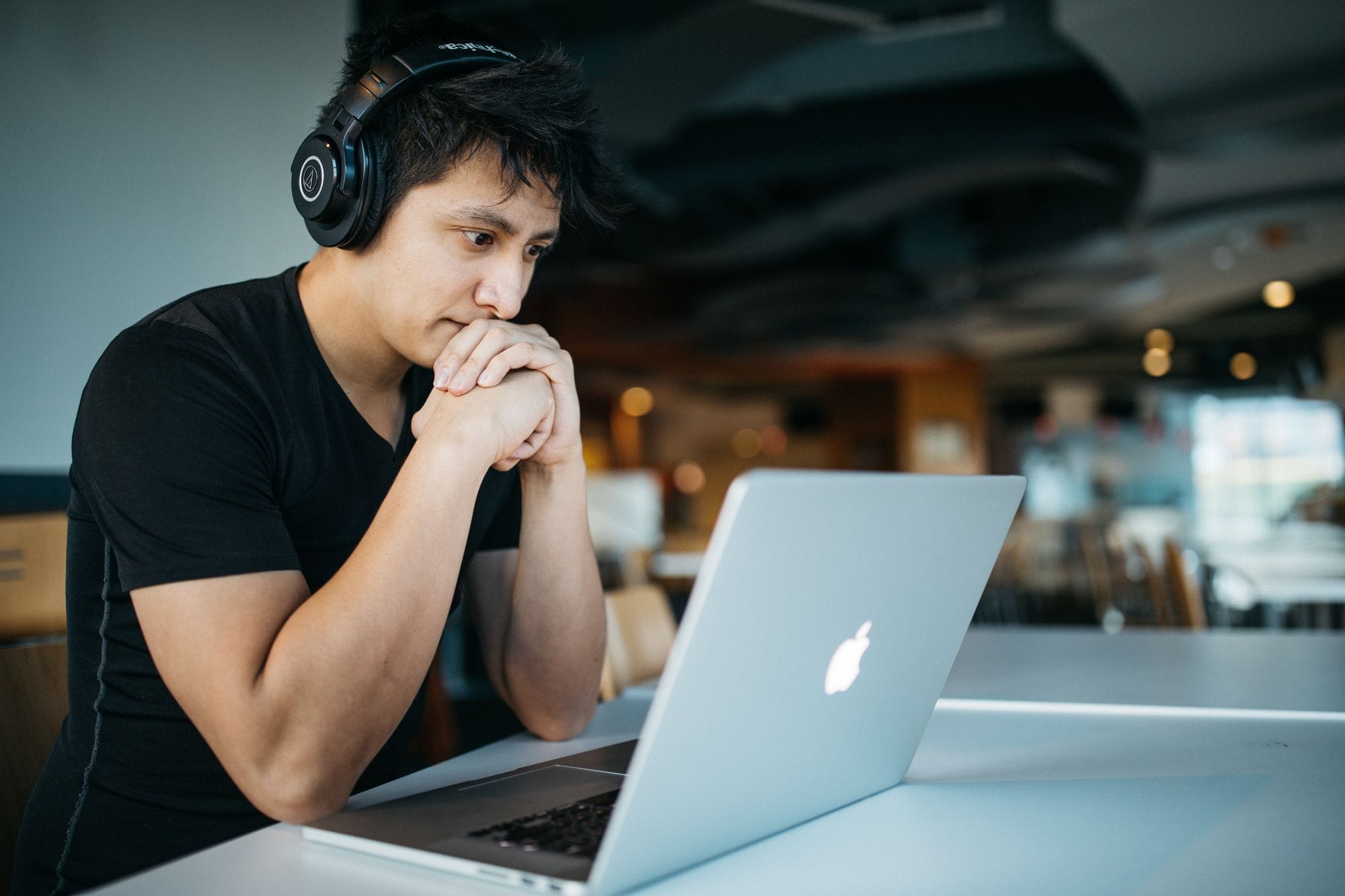 Un tânăr cu căști pe urechi privește gânditor ecranul unui laptop