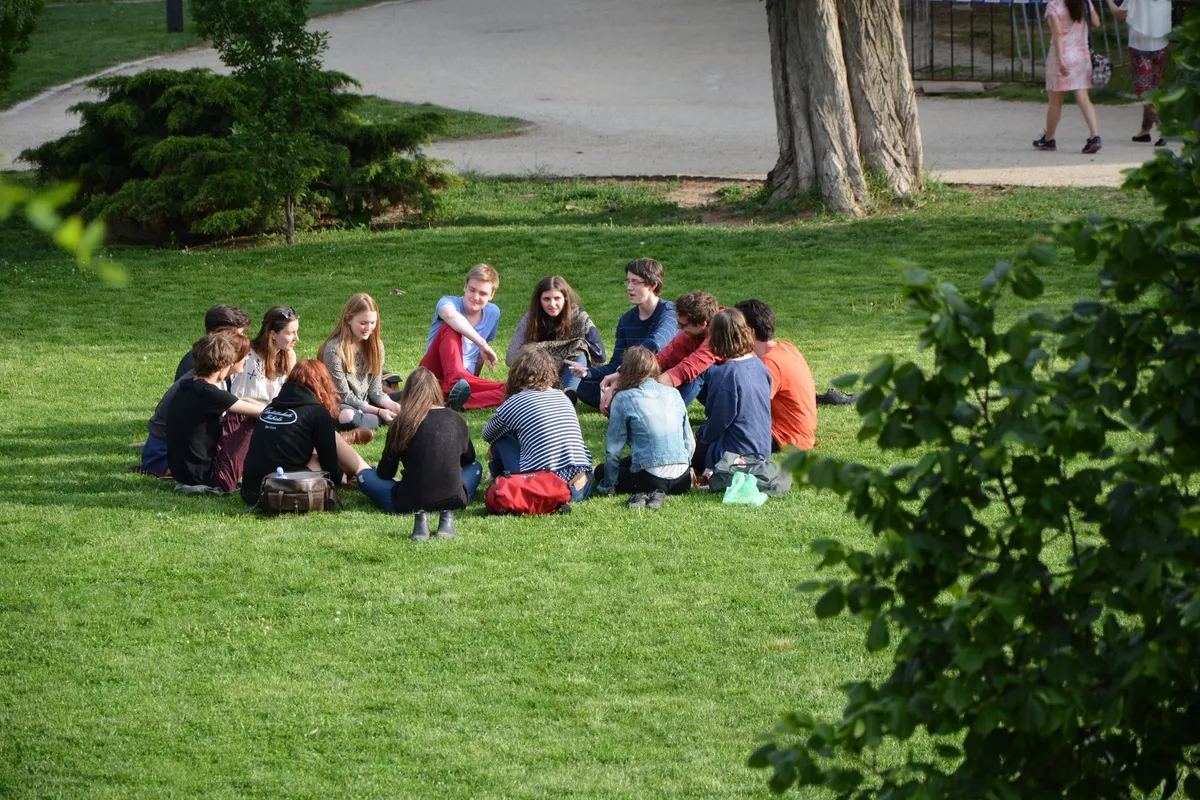 Un grup de tineri stă în cerc pe iarba unui parc și discută