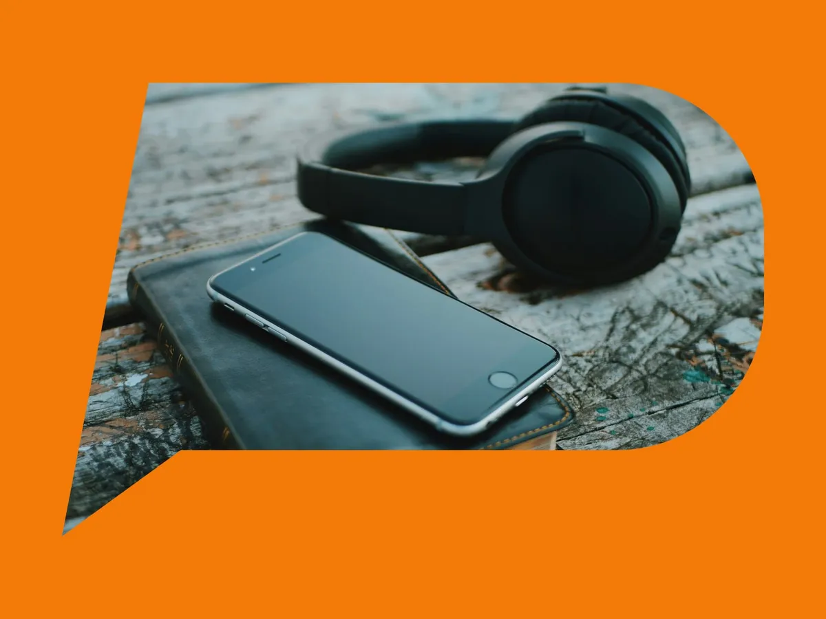 Un smartphone negru pe o Biblie închisă, lângă niște căști, pe lemn vechi