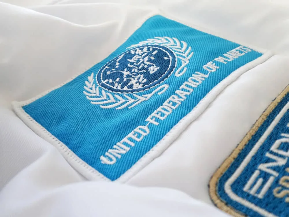 Ecuson albastru brodat cu emblema și inscripția „United Federation of Planets”, cusut pe un material alb