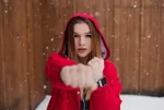 O tânără în geacă roșie cu glugă, cu un ceas inteligent la mână, întinde pumnul spre obiectiv, pe ninsoare